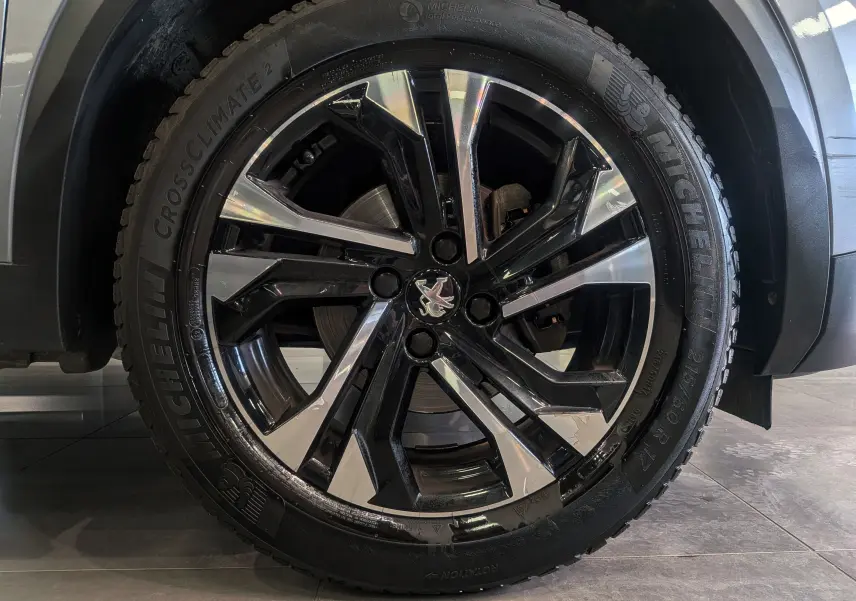 Gros plan sur la roue avant droite du Peugeot 2008 gris Artense, jante alliage noire et argentée avec logo lion central.