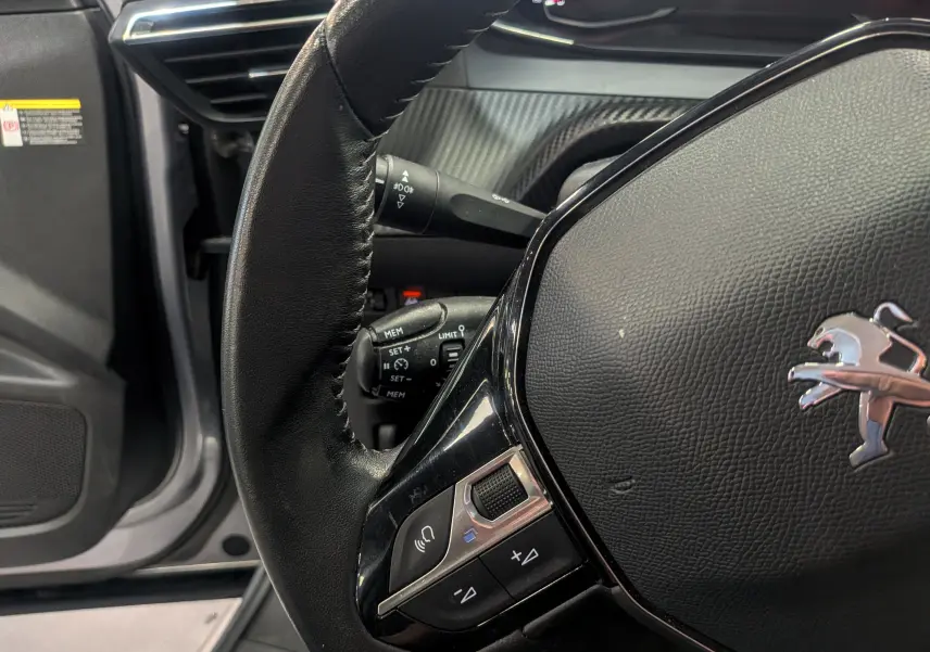 Gros plan sur le volant cuir noir du Peugeot 2008 gris Artense, avec commandes intégrées et tableau de bord partiel visible.