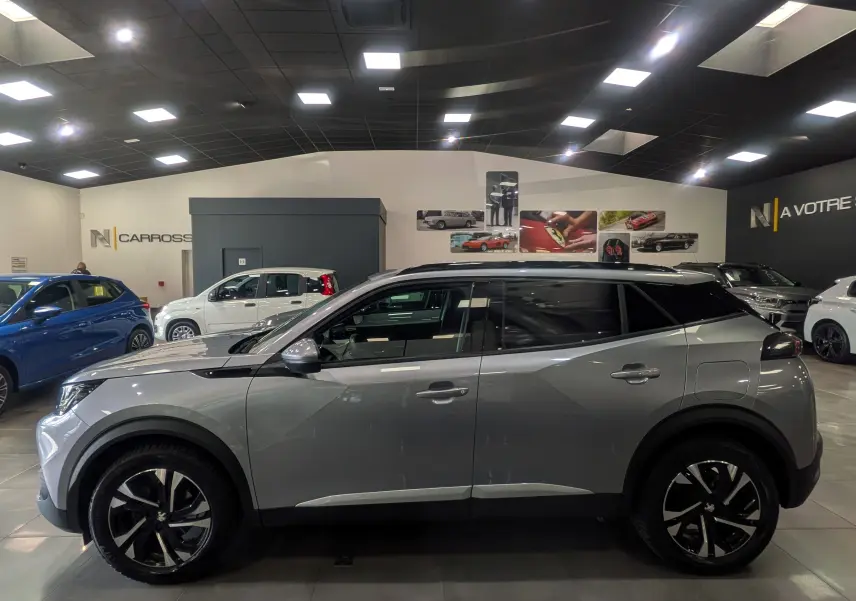 Peugeot 2008 gris Artense vue de profil côté gauche en intérieur, toit noir et jantes alliage bicolores.