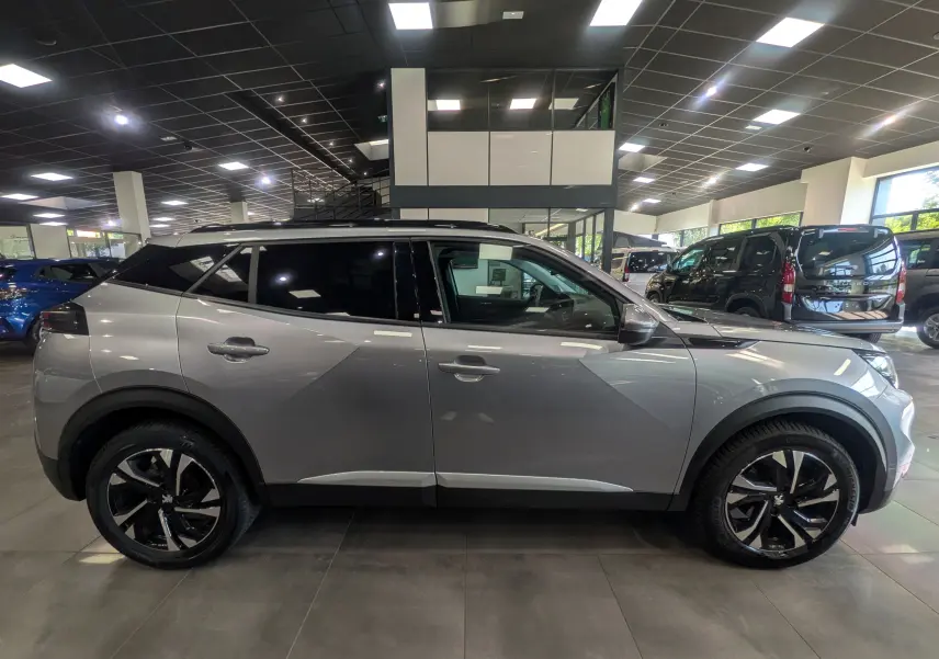 Vue de profil côté gauche d'un Peugeot 2008 gris Artense 2021 avec jantes noires et toit noir en concession.