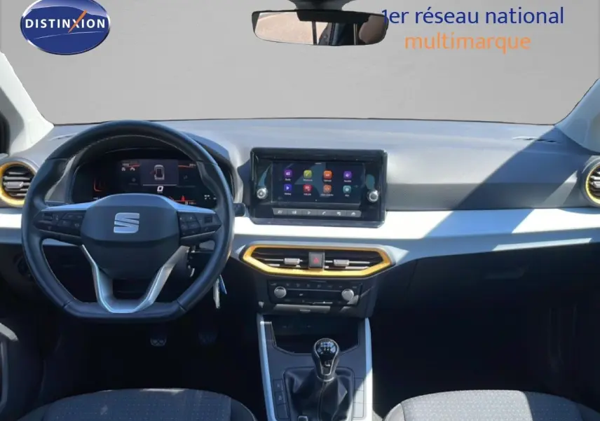 Vue intérieure avant du tableau de bord du SEAT Arona 2025, volant cuir, écran tactile et détails jaunes autour des aérateurs.