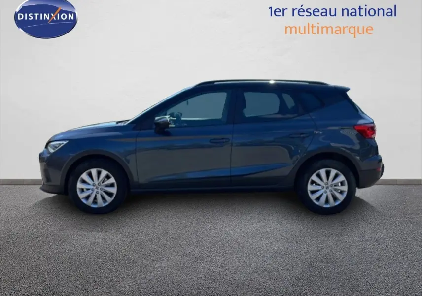Vue latérale gauche d'un SEAT Arona 2025 gris Magnetic Metal avec toit noir, posé sur sol gris devant un mur blanc.