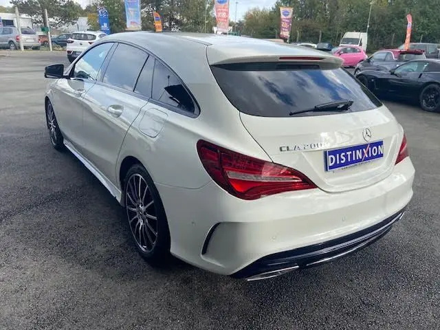 Vue 3/4 arrière droite d'une Mercedes CLA Shooting Brake 200D WhiteArt blanche avec jantes AMG bicolores et vitres teintées.