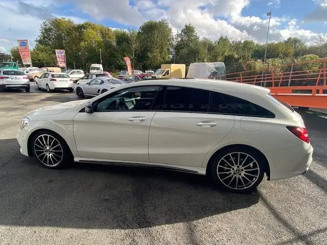 Vue latérale droite d'une Mercedes CLA Shooting Brake blanche avec jantes AMG noires et vitres teintées.