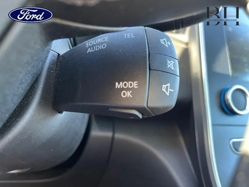 Gros plan sur la commande audio au volant d'une Renault Scenic blanc nacré/noir étoilé, avec boutons mode et volume.