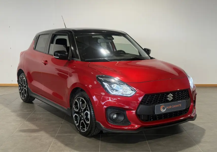 Suzuki Swift Sport rouge 3/4 avant droit avec toit noir et jantes alliage distinctives, en intérieur.