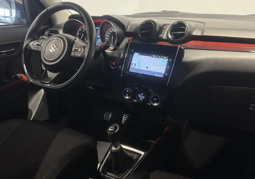Vue intérieure côté conducteur de la Suzuki Swift Sport rouge 2022, avec volant multifonction et écran tactile central.