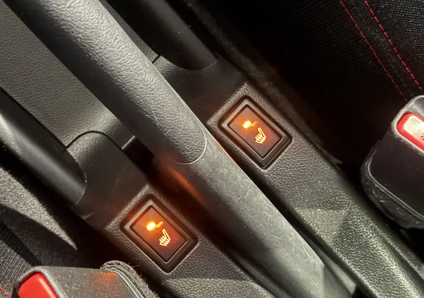 Gros plan sur les boutons de siège chauffant allumés au centre de la console d'une Suzuki Swift Sport rouge 2022.