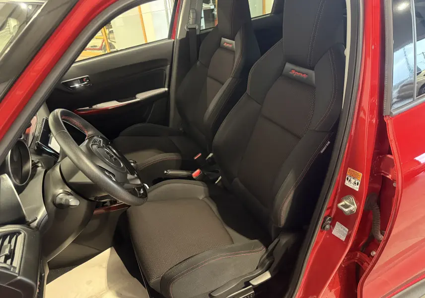 Vue intérieure côté conducteur de la Suzuki Swift Sport rouge 2022, sièges sport noirs avec surpiqûres rouges et logo Sport.