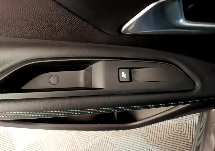 Gros plan sur la commande de lève-vitre côté conducteur avec surpiqûres bleues sur la garniture noire du Peugeot 3008 gris foncé.