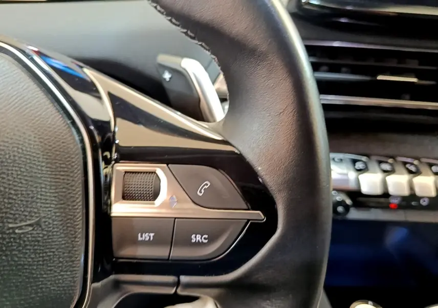 Gros plan sur les commandes gauche du volant cuir du Peugeot 3008 gris foncé, avec tableau de bord en arrière-plan.