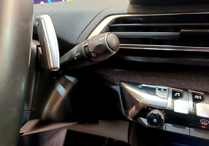 Détail du commodo d’essuie-glace et partie de la console centrale noire du Peugeot 3008 hybride gris foncé, vue intérieure.