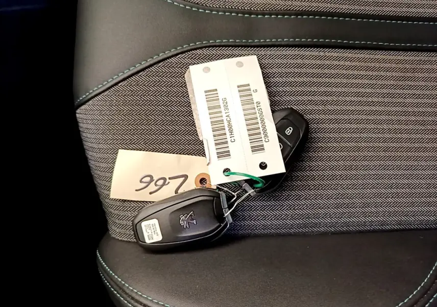 Gros plan sur la clé Peugeot posée sur un siège tissu gris foncé avec surpiqûres bleues.