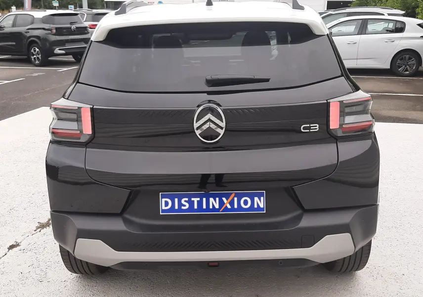 Vue arrière d'une Citroën C3 2025 noir perla avec toit blanc, feux LED et logo centré sur un parking.