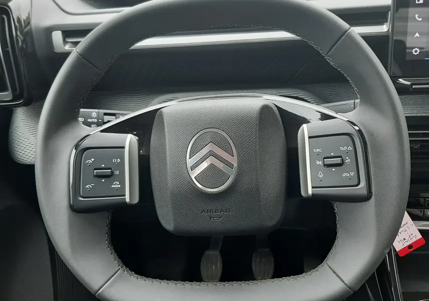Vue rapprochée du volant noir de la Citroën C3 2025, avec commandes intégrées et logo argenté central.