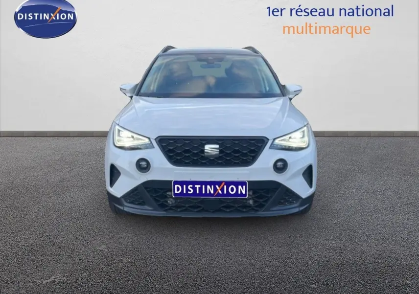 Vue frontale d'un SEAT Arona blanc avec toit gris, phares LED allumés et calandre noire distinctive.