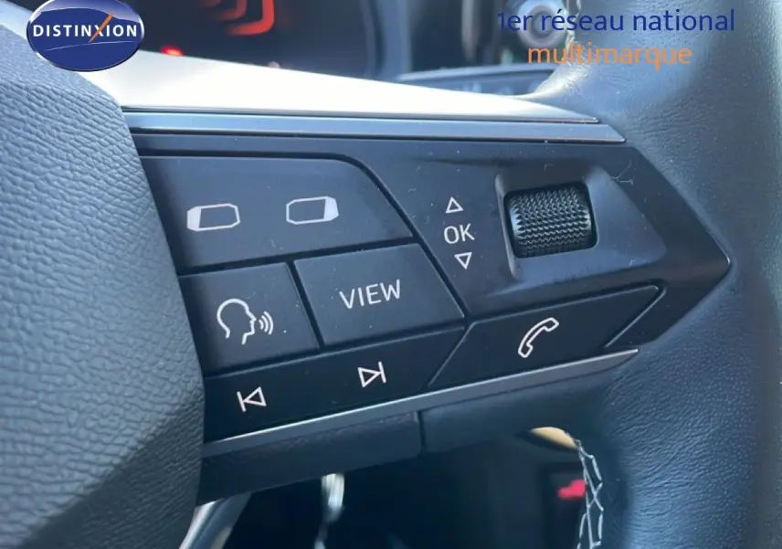 Gros plan sur les commandes au volant noir du SEAT Arona blanc 2025, avec boutons multifonctions et molette tactile.