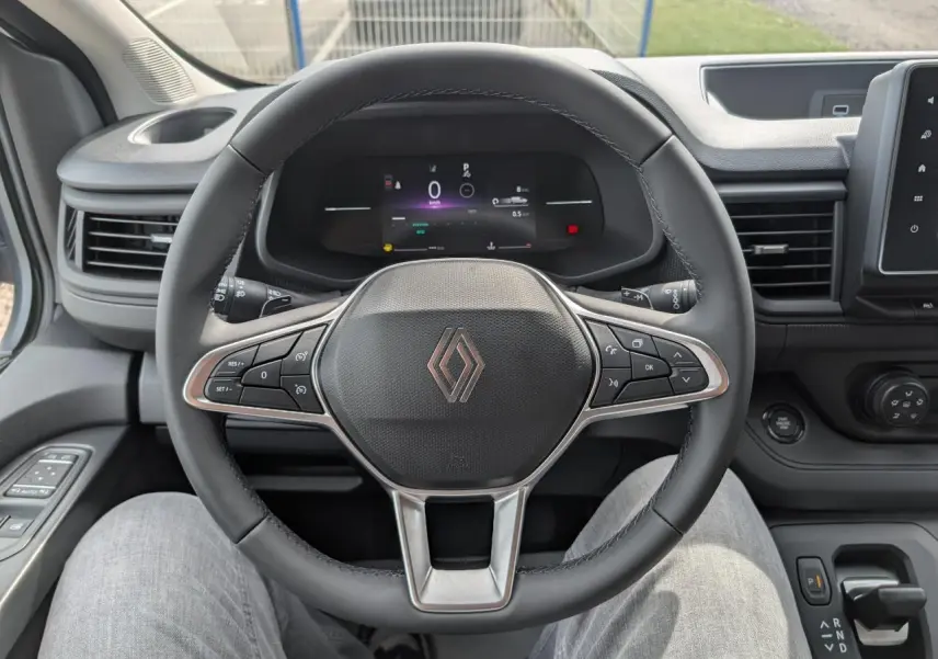 Vue rapprochée du volant noir et du combiné numérique du Renault Trafic Fourgon gris, avec commandes intégrées et tableau de bord moderne.