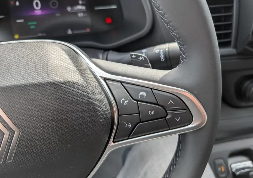 Gros plan sur les commandes à droite du volant noir du Renault Trafic Fourgon gris, avec affichage numérique en arrière-plan.