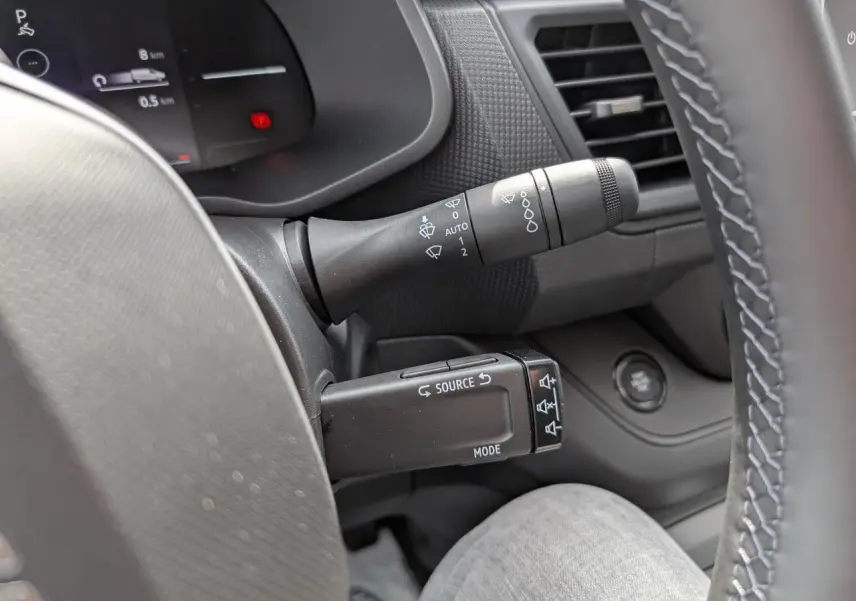 Gros plan sur la commande multifonction noire à gauche du volant dans l’habitacle gris du Renault Trafic Fourgon 2025.