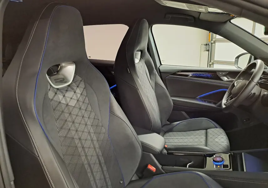 Vue intérieure côté droit du Volkswagen Tiguan 2.0 TDI R-Line 2025, sièges sport noirs avec surpiqûres bleues et éclairage d'ambiance.