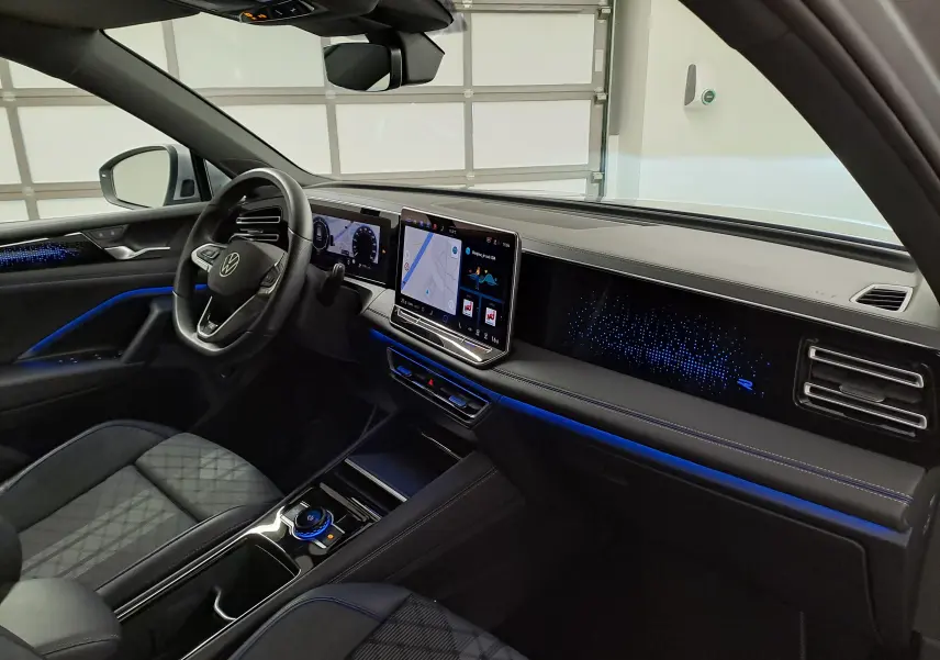 Vue intérieure côté conducteur du Volkswagen Tiguan 2025 avec éclairage d’ambiance bleu et écran tactile central.