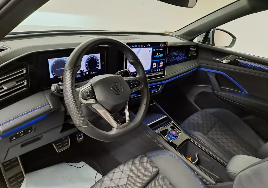 Vue intérieure côté conducteur du Volkswagen Tiguan 2.0 TDI 150 DSG7 R-Line avec éclairage d'ambiance bleu et écran tactile central.