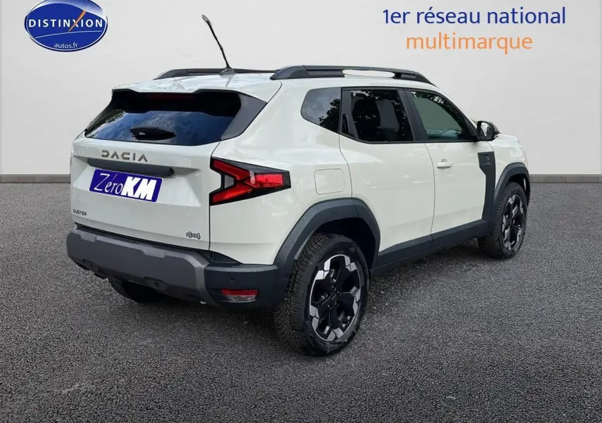 Vue 3/4 arrière droite du Dacia Duster 2025 couleur Sandstone avec jantes alu et barres de toit noires.