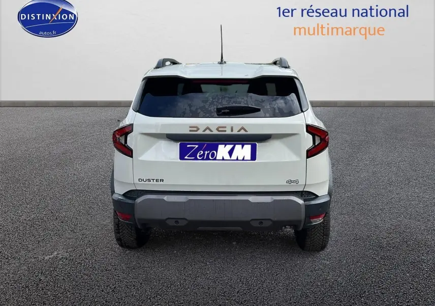 Vue arrière du Dacia Duster 2025 blanc Sandstone avec logo DACIA et badge 4x4 visible sur un sol goudronné.