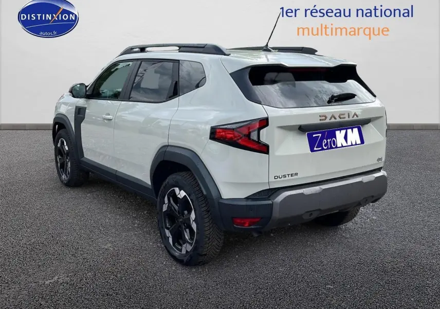 Vue 3/4 arrière droite du Dacia Duster 2025 couleur Sandstone avec barres de toit et jantes noires.