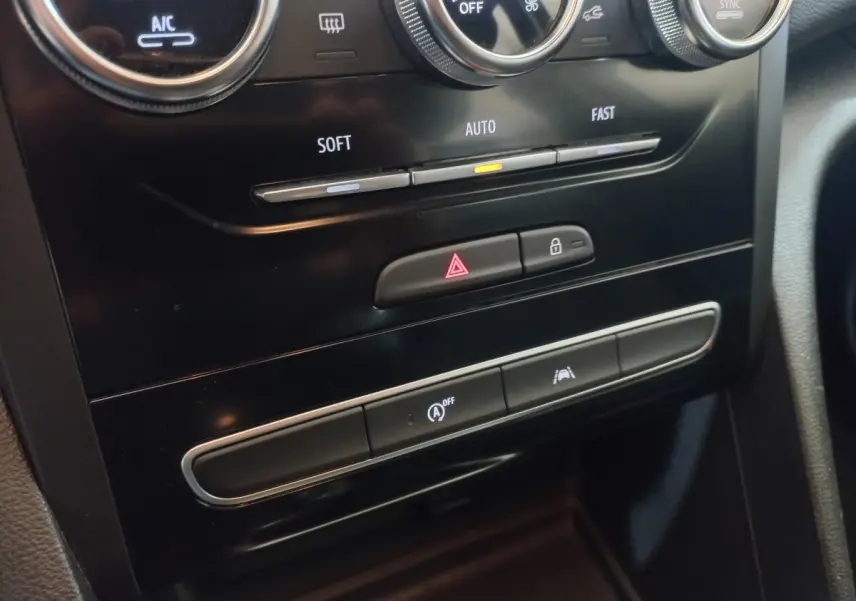 Gros plan sur la console centrale noire de la Renault Mégane Business TCe 115, montrant les commandes climatisation et boutons de sécurité.