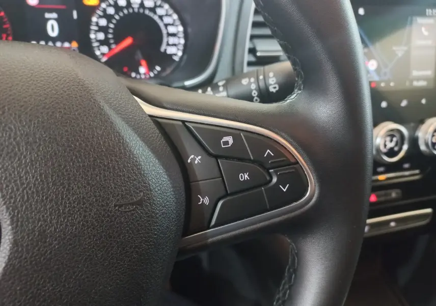 Gros plan sur le volant multifonctions noir de la Renault Mégane Business TCe 115, avec commandes et tableau de bord en arrière-plan.