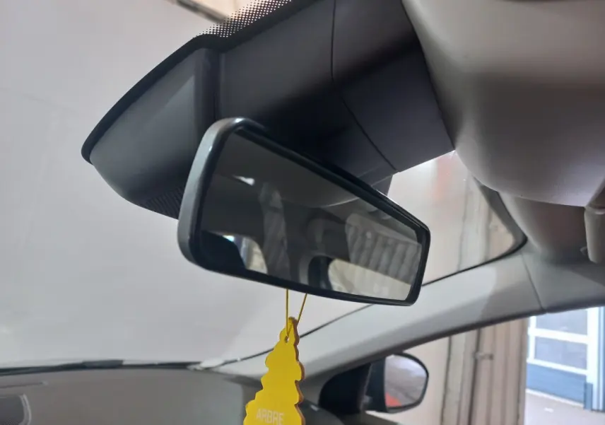 Vue intérieure centrée sur le rétroviseur intérieur d’une Renault Mégane gris foncé, avec un désodorisant jaune suspendu.