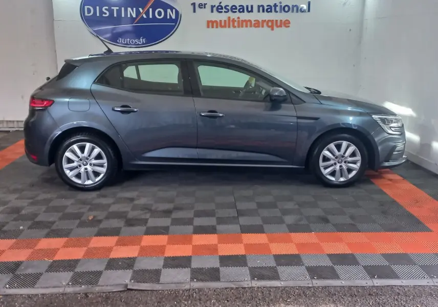 Profil côté gauche d'une Renault Mégane Business TCe 115 gris foncé, stationnée en intérieur sur sol à damiers noir et orange.