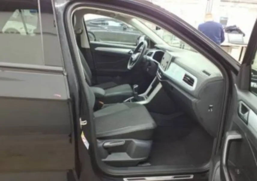 Vue intérieure côté conducteur d’un Volkswagen T-Roc noir 2025, montrant sièges tissu et tableau de bord moderne.