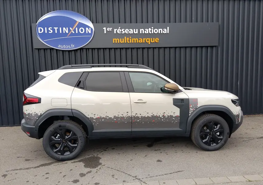 Vue de profil droit du Dacia Duster Hybrid-G 150 ch 4x4 en couleur Sandstone avec décor pixelisé gris et jantes noires.