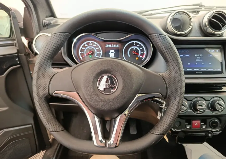 Vue rapprochée du volant noir perforé avec logo Aixam, tableau de bord et console centrale d'une Aixam Ambition blanche 2026.
