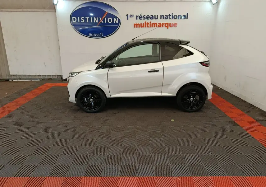 Vue de profil côté gauche d'une Aixam Ambition 0.5 City Coupe Sport blanche avec jantes noires dans un showroom.