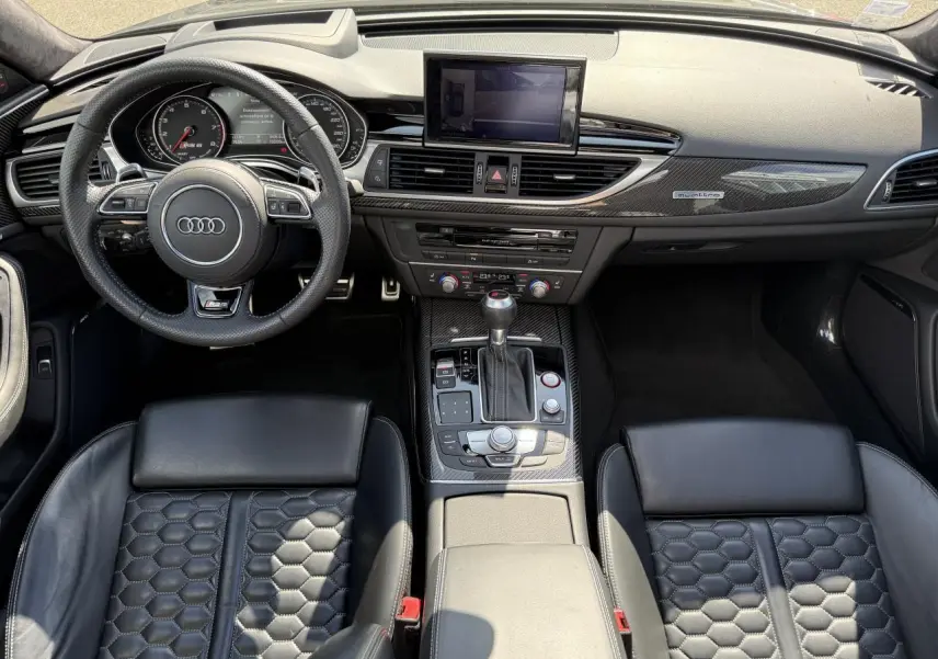 Vue intérieure avant de l'Audi RS6 Avant 2016 avec sellerie cuir noire à motif nid d'abeilles et tableau de bord carbone.