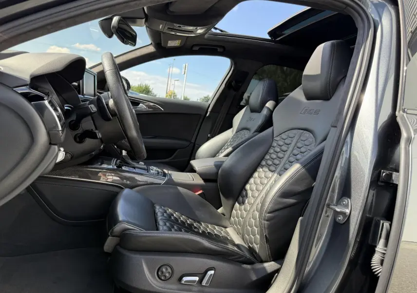 Intérieur avant droit de l'Audi RS6 Avant gris Daytona nacré, sièges sport en cuir noir embossé RS6 et toit ouvrant panoramique.