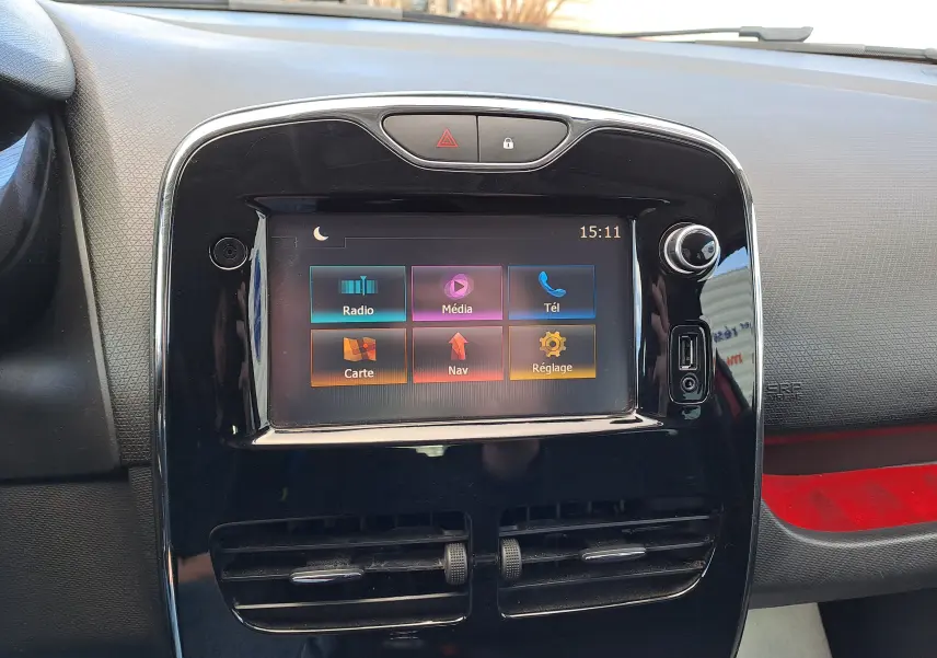 Vue rapprochée de l'écran tactile central noir brillant de la Renault Clio IV rouge, affichant les options radio, média, téléphone, carte, navigation et réglages.