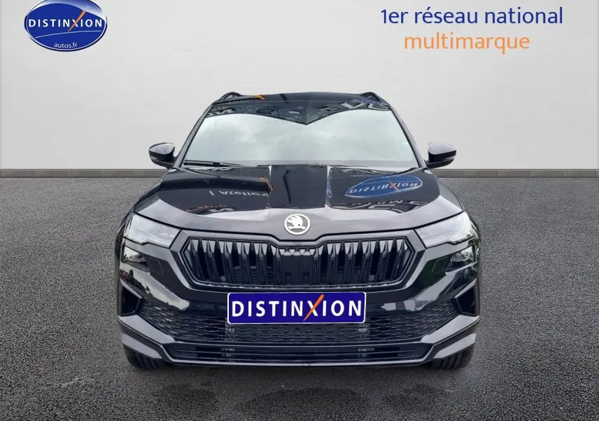 Vue frontale d'un Skoda Karoq noir 2025 avec calandre noire et logo centré, sur sol gris uniforme.