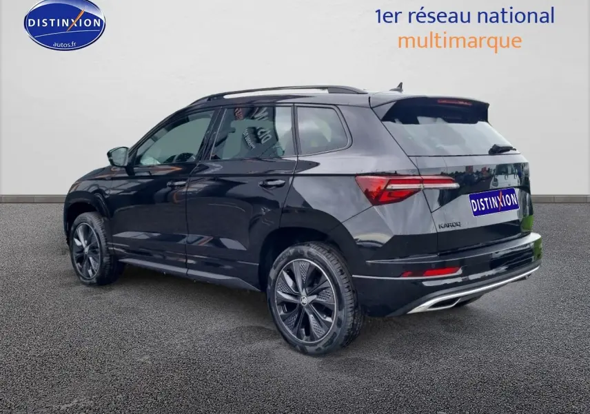 Vue 3/4 arrière droite d’un Skoda Karoq noir 2025 avec jantes alu et barres de toit visibles.