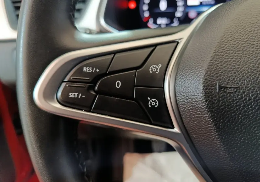 Gros plan sur les commandes de régulateur de vitesse au volant du Renault Captur rouge, intérieur visible en arrière-plan.