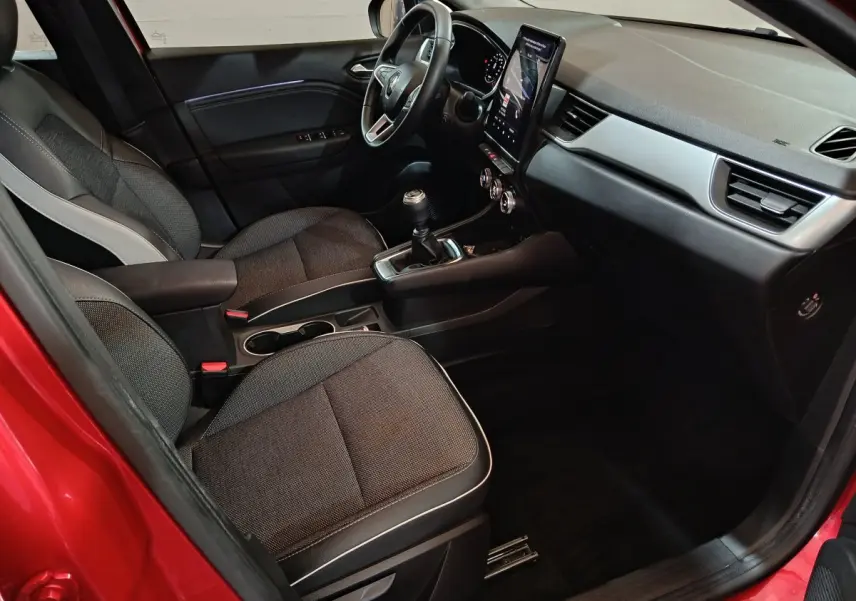 Intérieur Renault Captur 2024 rouge, vue côté conducteur, volant multifonctions et écran tactile vertical.