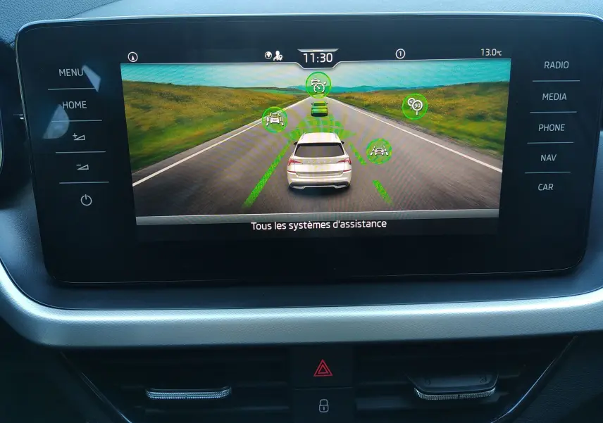 Écran central du Skoda Kamiq 2023 montrant l'affichage des systèmes d'assistance à la conduite avec vue arrière du véhicule gris.