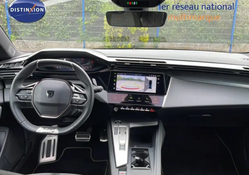 Vue intérieure avant du tableau de bord et volant noir de la Peugeot 408 1.2 Hybrid 145ch GT avec écran tactile affichant la caméra de recul.