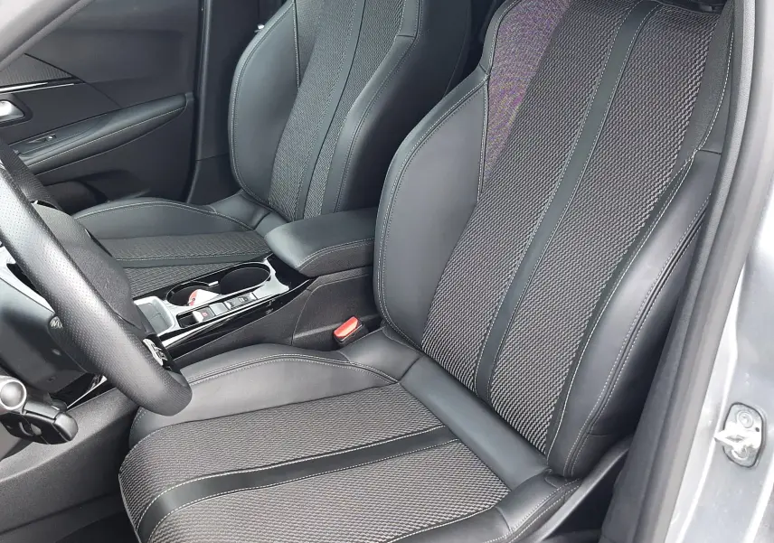 Vue intérieure côté conducteur de la Peugeot 208 GT 1.2 essence 2025, sièges tissu et cuir gris avec surpiqûres contrastées.