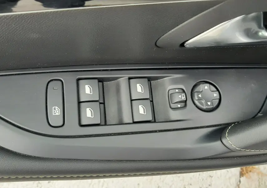 Gros plan sur les commandes des vitres et rétroviseurs côté conducteur d'une Peugeot 208 gris Artense, avec surpiqûres vertes.