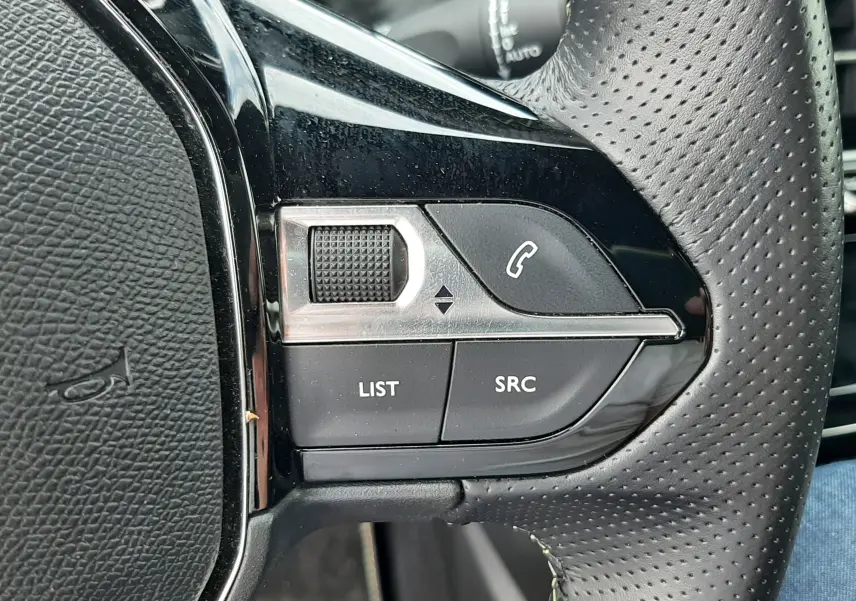 Gros plan sur les commandes gauche du volant perforé noir de la Peugeot 208 gris Artense, boutons LIST et SRC visibles.